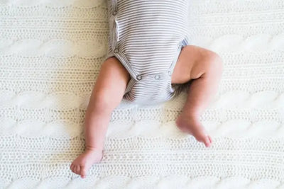 A baby boy sitting in a crib in his organic and American made bodysuit.