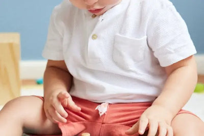 A baby boy sitting playing with toys while wearing a white tee shirt.