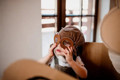 A baby wearing an aviator costume mask.