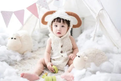 A baby girl is wearing a white, sheep themed hoodie.