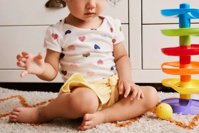 A baby girl plays with toys while wearing a heart designed t-shirt.