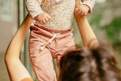 A baby, wearing American-made pants, is being held by a mother.