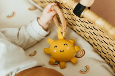 A baby holds a baby rattler shaped like the sun.