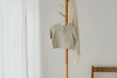 An American-made baby shirt hangs from a hanger on a coat rack.