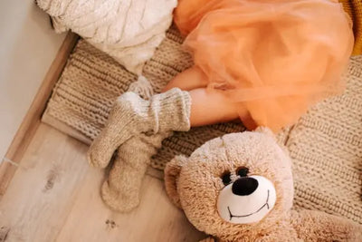 A girl is sitting in her orange skirt next to a teddy bear.