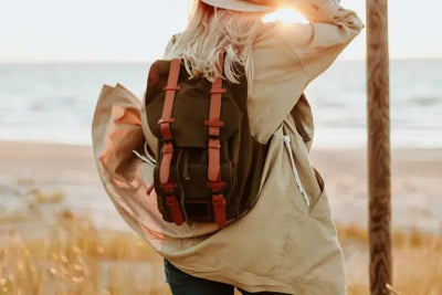 A woman standing at the beach wearing a backpack.