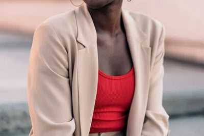 A woman sits in a city wearing a beige American-made blazer.