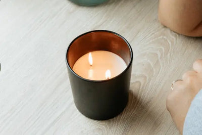 A soy candle that was hand poured in the USA sits on a table providing a pleasant aroma for the person in the room. 