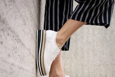 A woman leaning on a wall wearing a black and white striped pair of capris that were made in America.