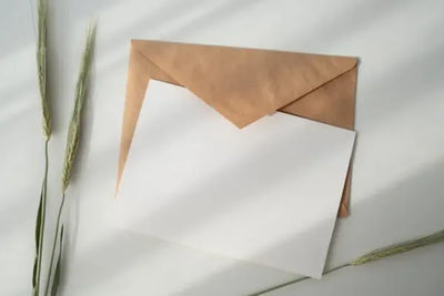 A brown envelope partially open with a blank white card beside it, surrounded by grass blades.