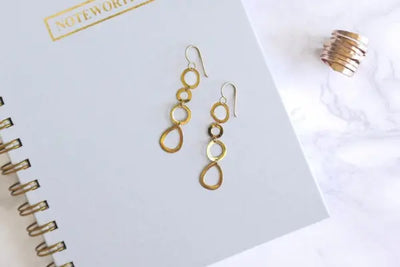 Two gold chandelier earrings on a notebook.