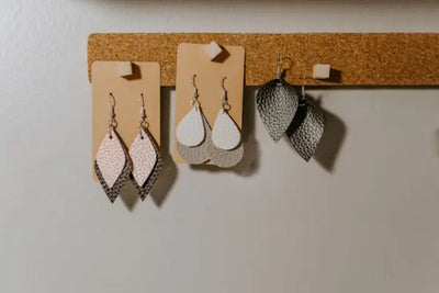 Three pairs of handcrafted earrings sit on a shelf. 