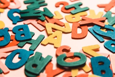 Colorful wooden or felt alphabet letters scattered on a light surface. Vibrant reds, blues, yellows, and pinks create a playful, educational vibe, perfect for learning or creative play themes.
