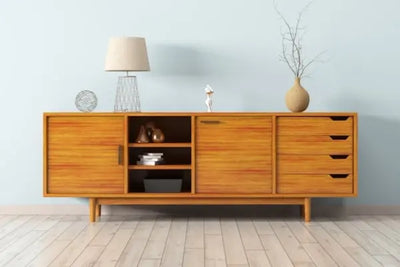 Mid-century wooden sideboard against a light blue wall, styled with a wire sphere, glass-base lamp, small white sculpture, and a vase with branches; open shelves and drawers show minimal decor.