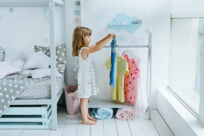 A girl wearing a white dress holds up two colorful shirts that were made in America. 