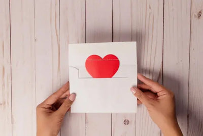 Two hands holding a white envelope with a red heart peeking out. 