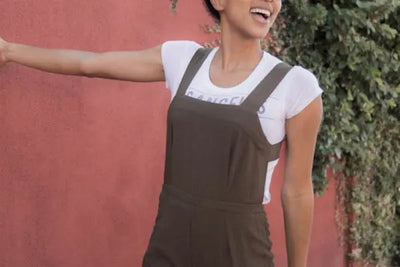 A woman wearing an American-made white t-shirt under a brown overall.