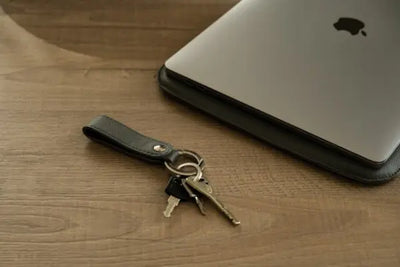 A black leather keychain with American made leather sits next to an Apple computer.