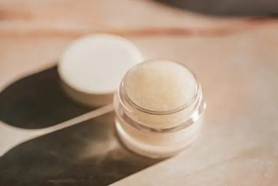 A jar of lip scrubs sits opened on a brown table with the lid to the jar's side. 