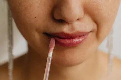 A woman smirks as she puts lip gloss on her lips with products that were carefully crafted in America. 