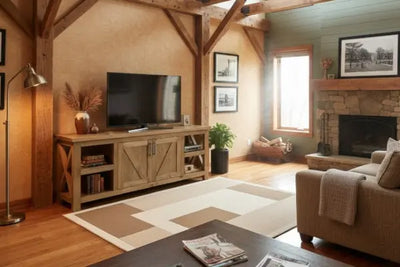 A rustic living room with exposed wooden beams, a stone fireplace, and natural wood furniture. Features include a beige sofa, entertainment console, coffee table, and warm lighting for a cozy vibe.