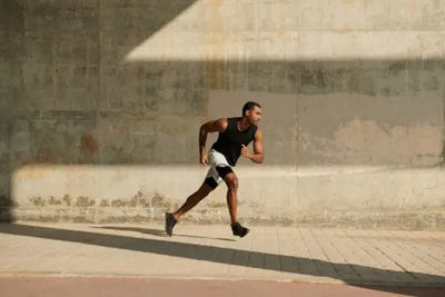 A man wearing white shorts and a black tank top made in the USA runs around a sports complex.