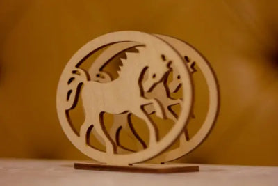 Intricately laser-cut wooden napkin holder featuring circular designs with winged horse silhouettes. Made of light wood with a natural finish, set on a simple base against a warm golden-brown backdrop.