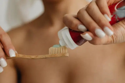 A woman putting tooth paste on a tooth brush.