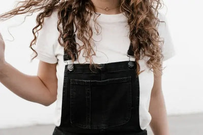 A woman wearing a white t-shirt with an American-made, black overall. 