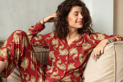 A woman wearing red, American-made pajamas plays with her hair while sitting on a brown couch.