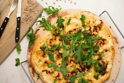 Pizza on a brown pizza and silver steel stone that was made in America. The mozzarella pizza is perfectly cooked and layered with spinach. 