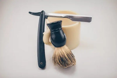 A black shaving brush and silver shaver that were made in America cleanly sit on a counter waiting to be used for grooming. 