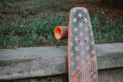 An orange and blue skateboard with starts on it.