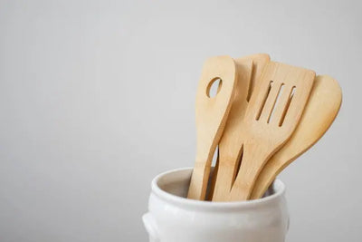 Wooden cooking utensils, including a spatula and spoon, in a white jar.