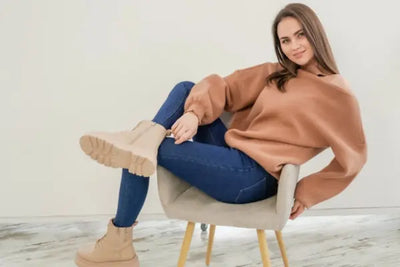 A woman sits in a beige chair with her American made, brown sweatshirt. 