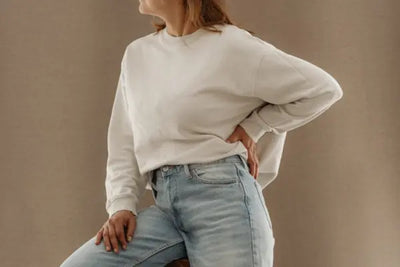 A woman in jeans is wearing a white, organic, American-made sweatshirt.