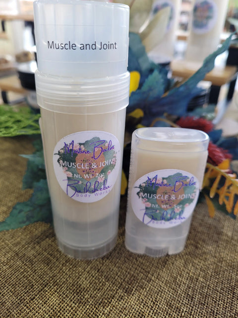 Two clear plastic tubes of Moisture Balm - Muscle and Joint from Bathsheba Body Works, featuring colorful labels, organic ingredients, and two sizes, are displayed on a textured surface with a decorative background.