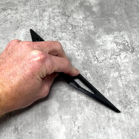 A left hand holds the Chatelet Manufacturing 10-Inch Plastic Paint Guide and Trim Guard with angular cutouts against a textured gray surface, ideal for precision painting on DIY and professional jobs.