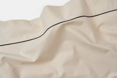 A close-up of the Cotton Piping Design Bed Sheet Set by American Blossom Linens, showcasing cream-colored cotton sheets with a single thin black line and subtle wrinkles and folds.