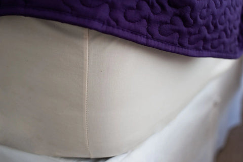 A close-up of a cream mannequin torso draped with a luxurious, purple Cotton Single [Separate] Fitted Bed Sheet by American Blossom Linens, showing its textured, quilted fabric reminiscent of USA-grown cotton.