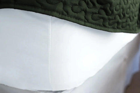 A close-up of the lower half of a mannequin showcases luxurious white Cotton Single Fitted Bed Sheet by American Blossom Linens, evoking the comfort of USA-grown cotton, paired with a dark green quilted garment above the waist.