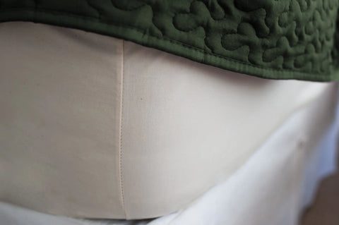 Close-up of a luxurious, light-colored fabric with a vertical seam, partially covered by green quilted material—crafted from USA cotton. Shown: Cotton Single [Separate] Fitted Bed Sheet by American Blossom Linens.