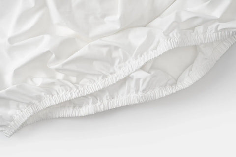 Close-up of the American Blossom Linens Cotton Single [Separate] Fitted Bed Sheet with elastic edges, slightly wrinkled and resting on a white surface—made from USA grown cotton.