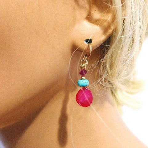 A close-up shows a womans ear with blonde hair, wearing Alexa Martha Designs 14 KT Gold Filled Wire Wrapped Pink and Turquoise Drop Gemstone Earrings. The earrings feature turquoise, a small red bead, and a larger hot pink chalcedony teardrop.