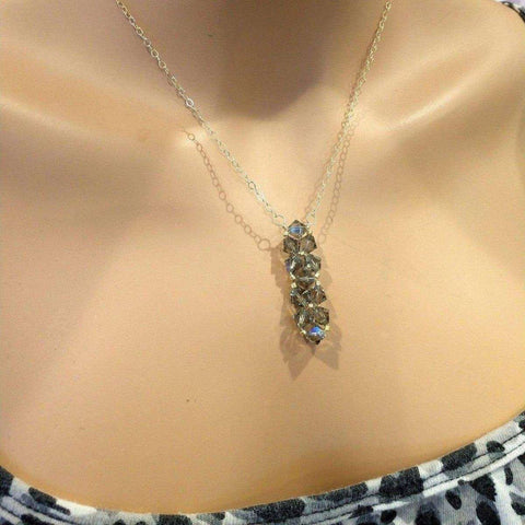 A close-up of a person’s neck wearing the Gold Wire Bead-Woven Rock Candy Crystal Bar Necklace by Alexa Martha Designs. The necklace features five clear crystals arranged vertically on a handmade gold chain, paired with a patterned top.