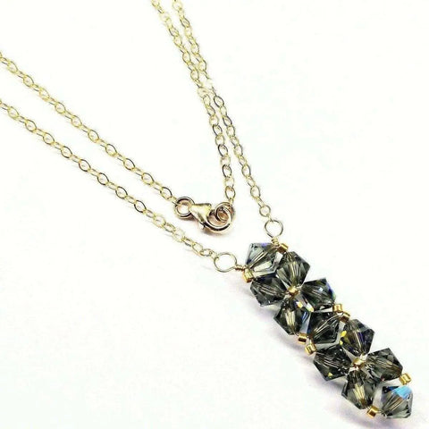 The Gold Wire Bead-Woven Rock Candy Crystal Bar Necklace by Alexa Martha Designs features six faceted smoky gray Swarovski crystal cubes stacked vertically, set on a 14K gold-filled chain with a lobster clasp. Handmade in Montana.