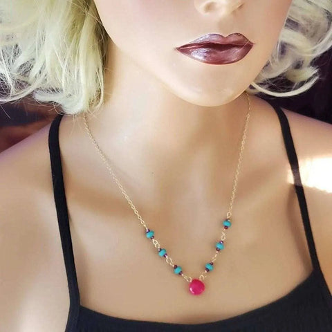 A mannequin with blonde, curly hair wears a black top and the Alexa Martha Designs Gold Filled Pink Chalcedony Turquoise Gemstone Drop Necklace, featuring small turquoise beads and a central pink chalcedony bead.