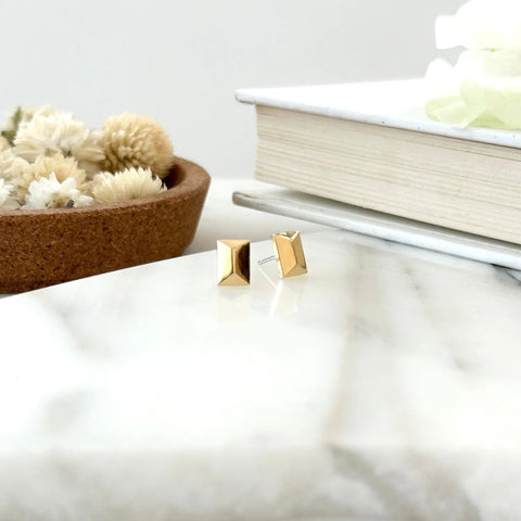 The GOLD CANAL STUDS by Sarah Cecelia are displayed on a white marble surface, accented by a dish of dried flowers and stacked books for an elegant, minimalist look.
