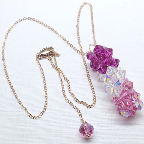 The 14K Rose Gold Fill Super Sparkly Mom Crystal Pillar Pendant Necklace by Alexa Martha Designs features stacked purple, clear, and pink Swarovski crystal beads, finished with a purple accent bead—beautifully displayed on a white background.