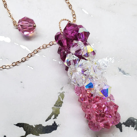 The Alexa Martha Designs 14 K Rose Gold Fill Super Sparkly Mom Crystal Pillar Pendant Necklace rests on a white marbled surface, with a matching crystal bead nearby.